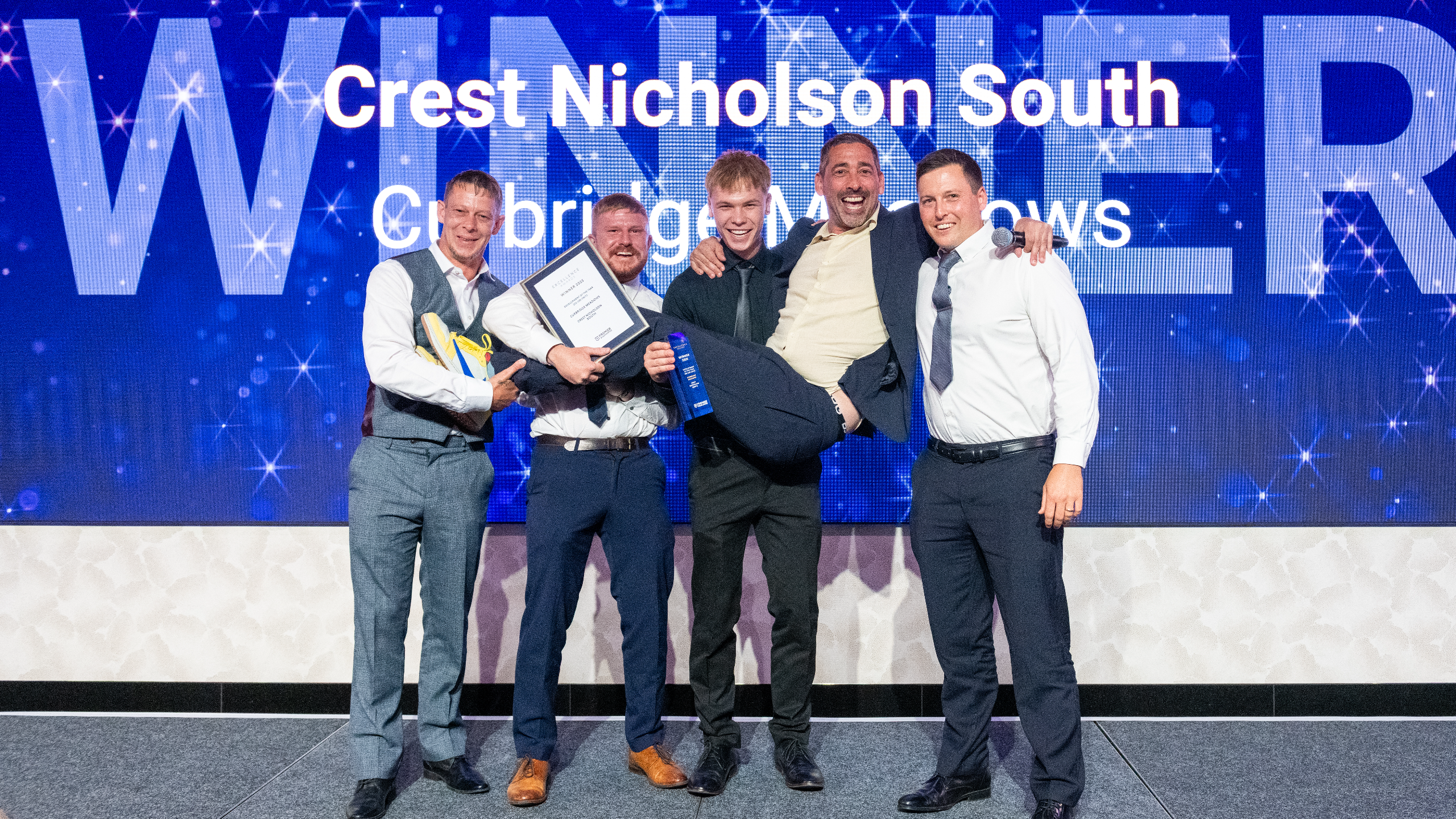 Excellence Awards 2025 10 Five men celebrate on stage, holding awards with a bright blue backdrop displaying "WINNER" and "Crest Nicholson South.