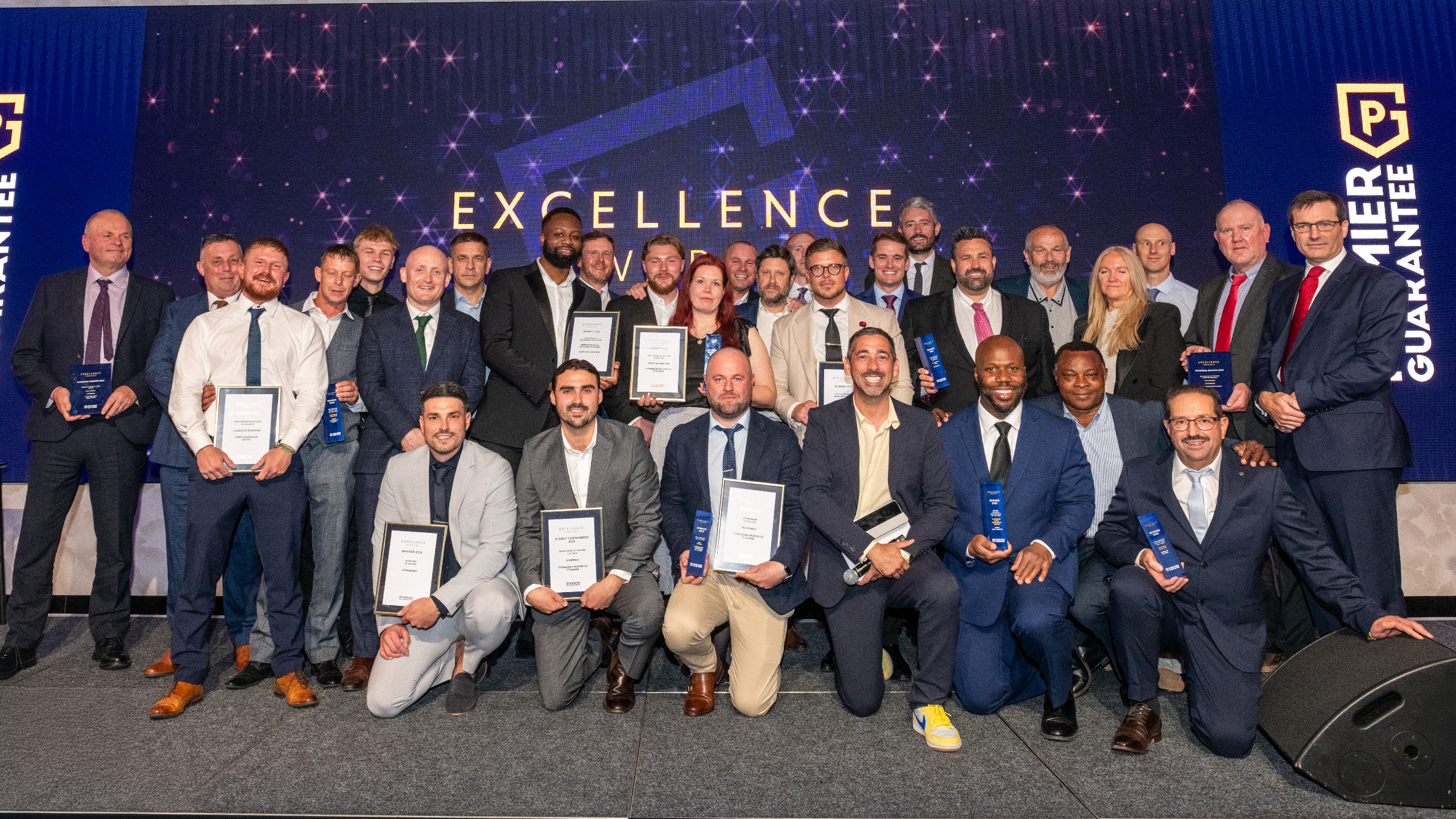 Excellence Awards 2025 12 A group of people in formal attire posing with awards on a stage decorated with a starry backdrop.