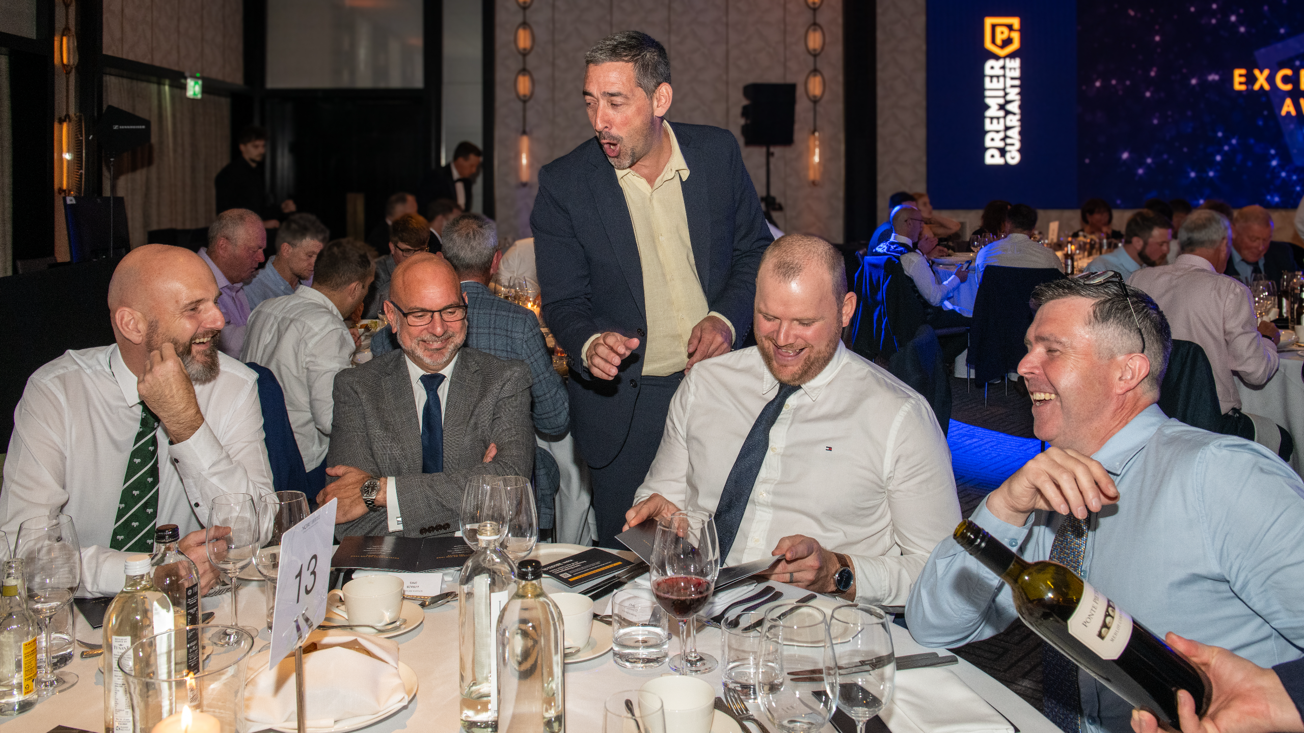 Excellence Awards 2025 2 A group of men seated at a dining table with drinks and menus, engaged in conversation at a formal event.