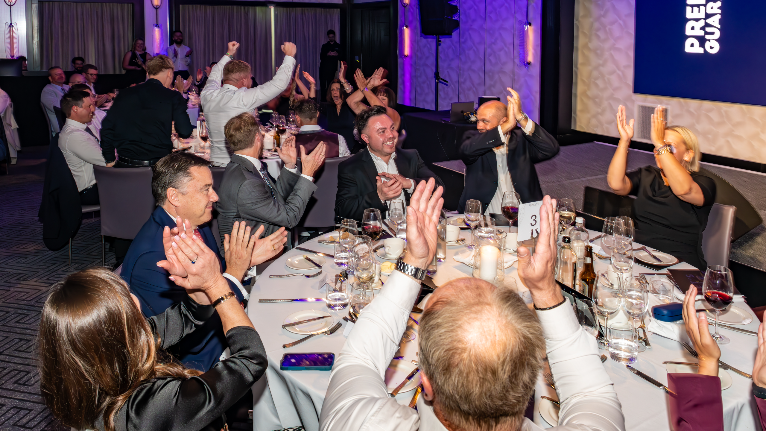 Excellence Awards 2025 5 A group of people at a dining table celebrating, clapping hands, with drinks and plates on the table.