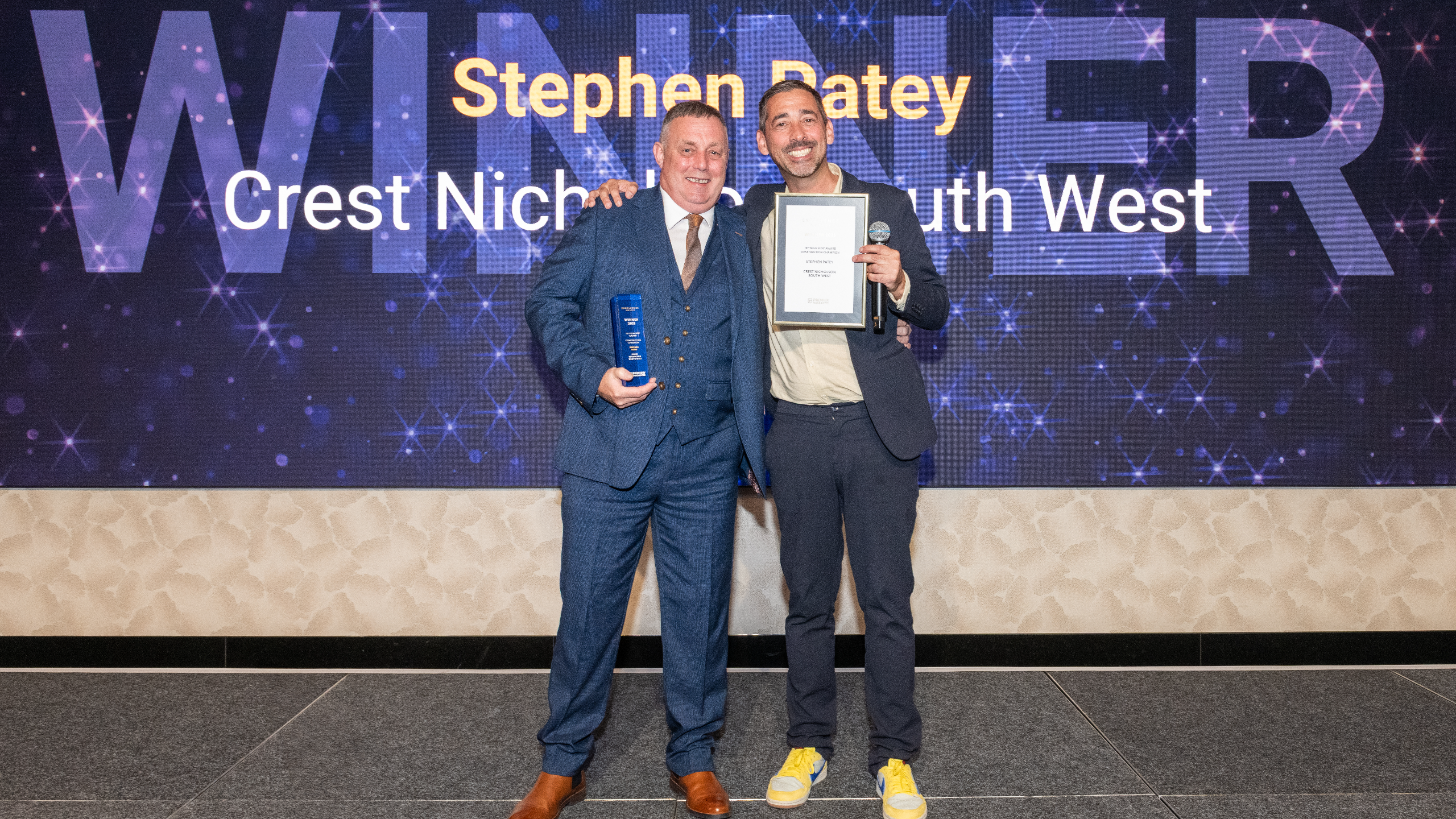 Excellence Awards 2025 7 Two men stand together holding an award and a certificate in front of a "Winner" backdrop.