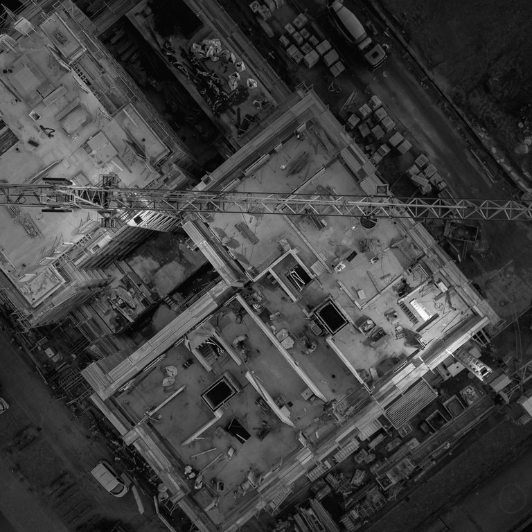 Aerial view of two construction sites with cranes, building materials, and parked vehicles.
