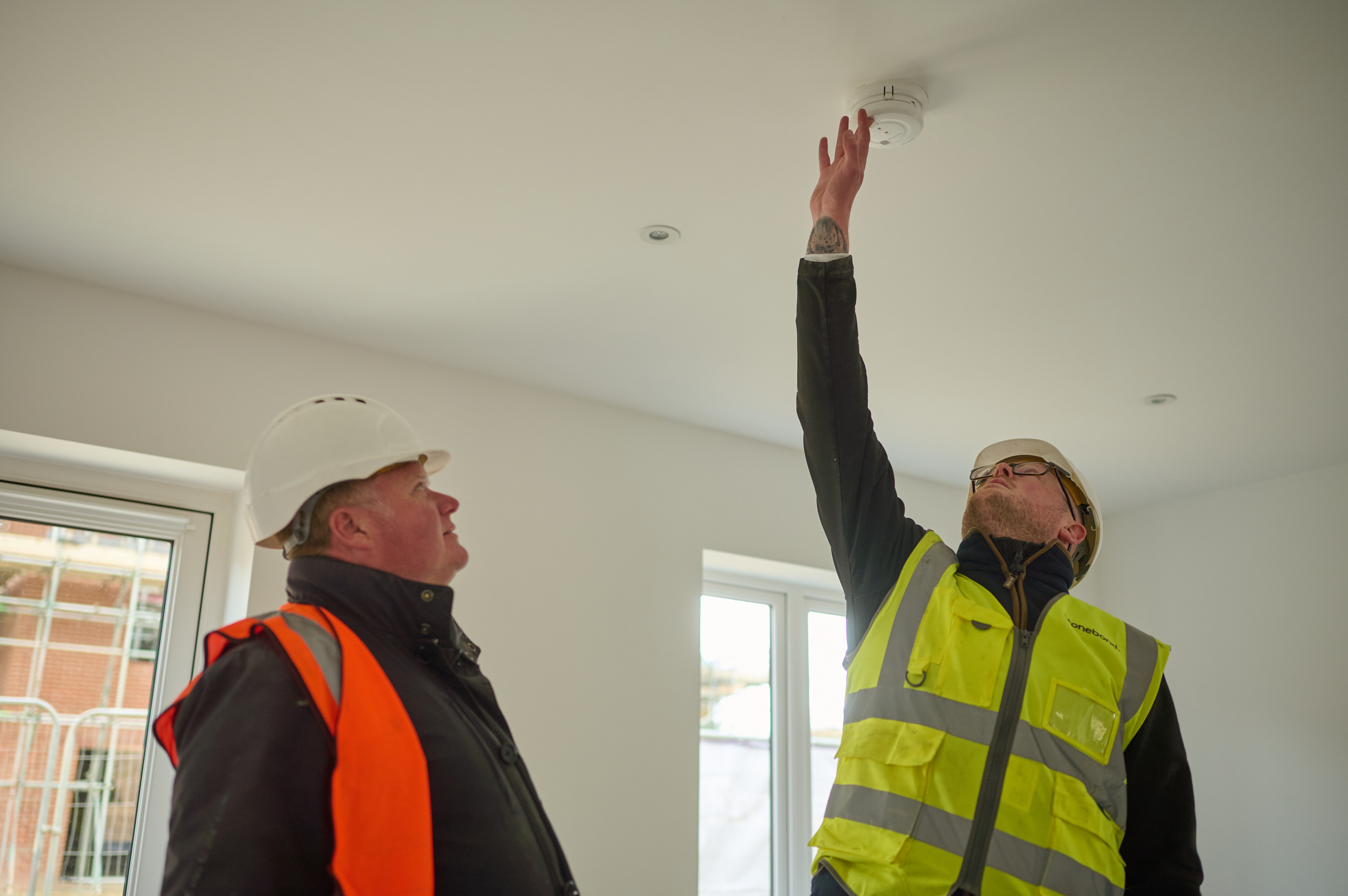 Defects Insurance Period Inspectors looking at smoke detector in new build home