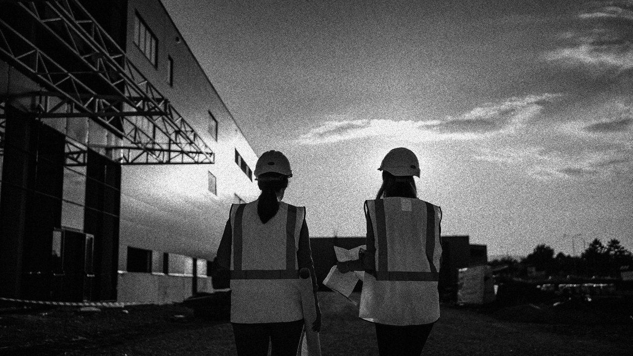 Two women in hard hats at a construction site Two women in safety vests and helmets walk away from a construction site at sunset.