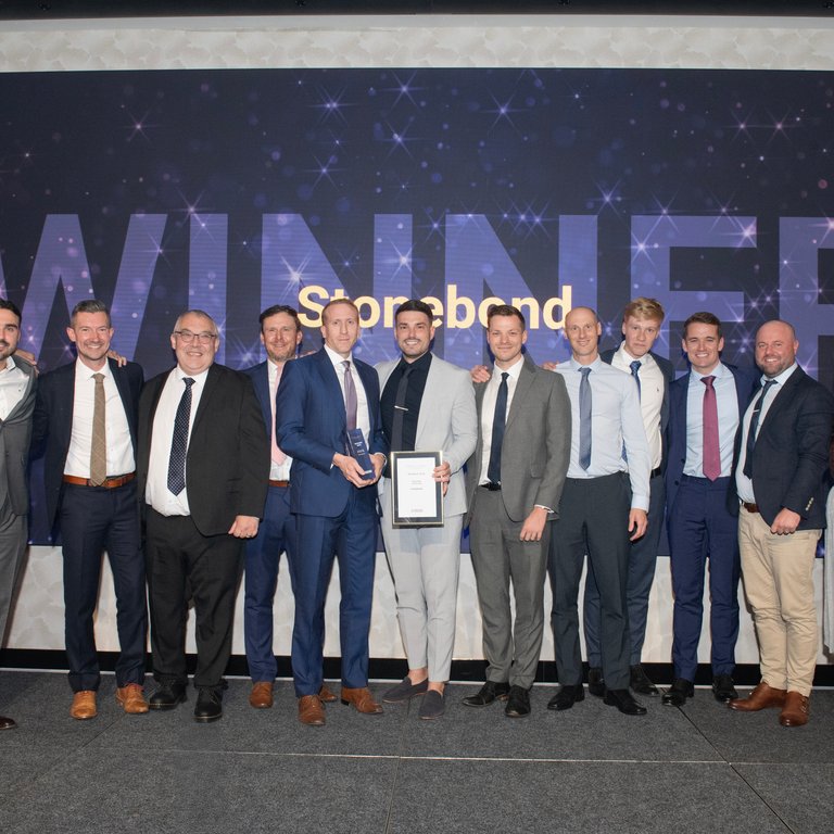 A group of people on stage celebrating an award with a large screen displaying "WINNER Stonebond" in the background.