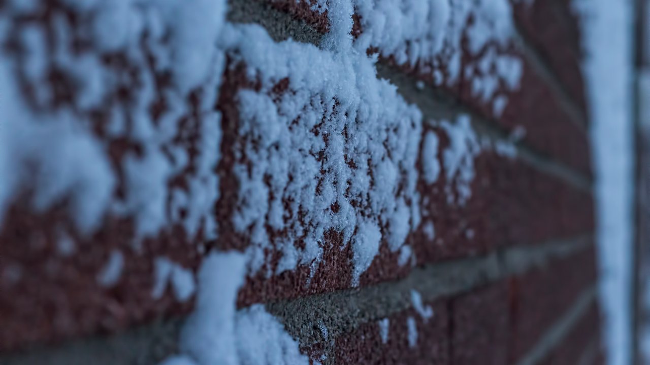 A close-up image of a brick wall with patches of snow on it.