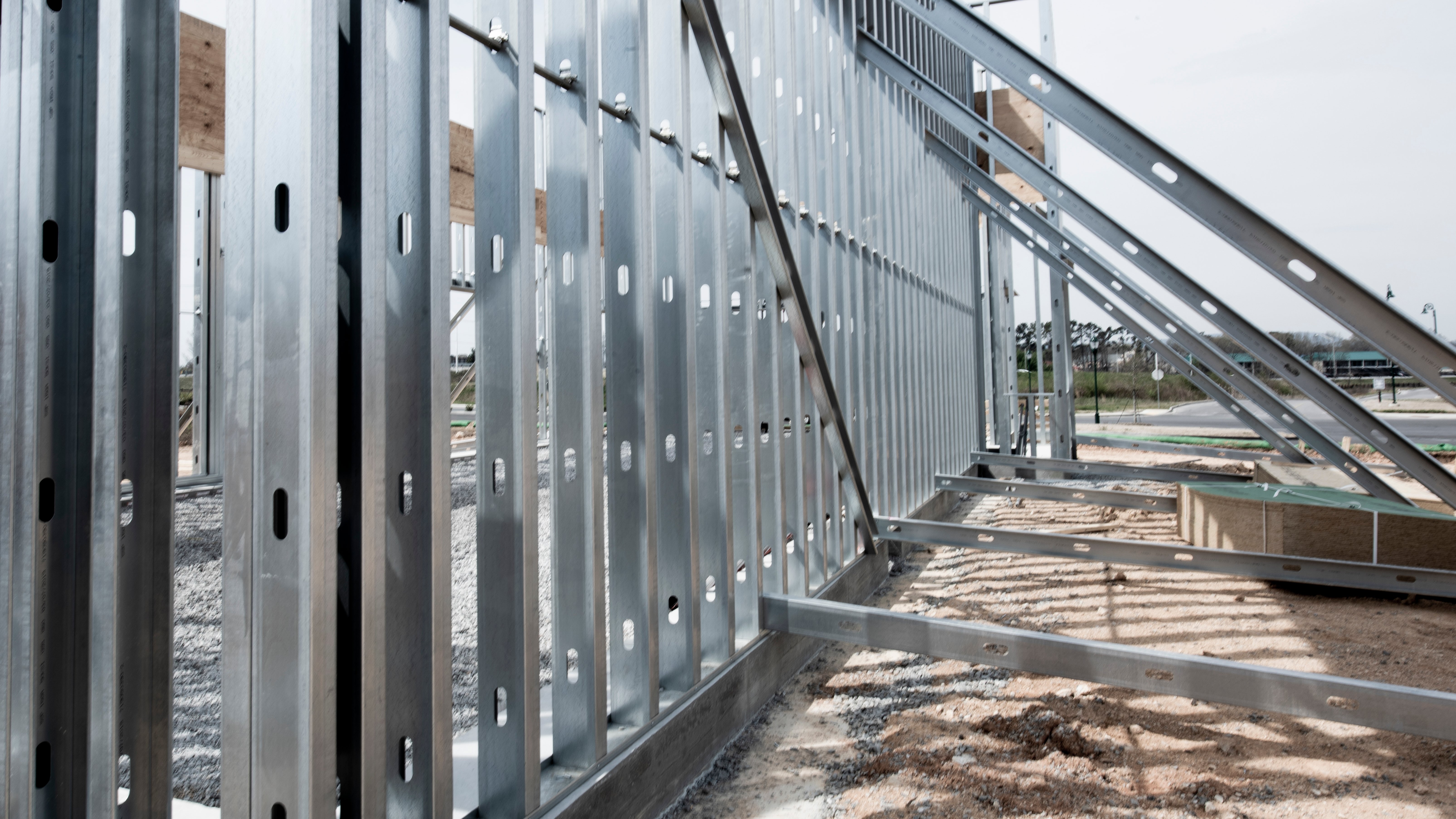 Close-up view of a steel frame structure under construction, showing metal studs, beams, and diagonal braces at a modern building site.