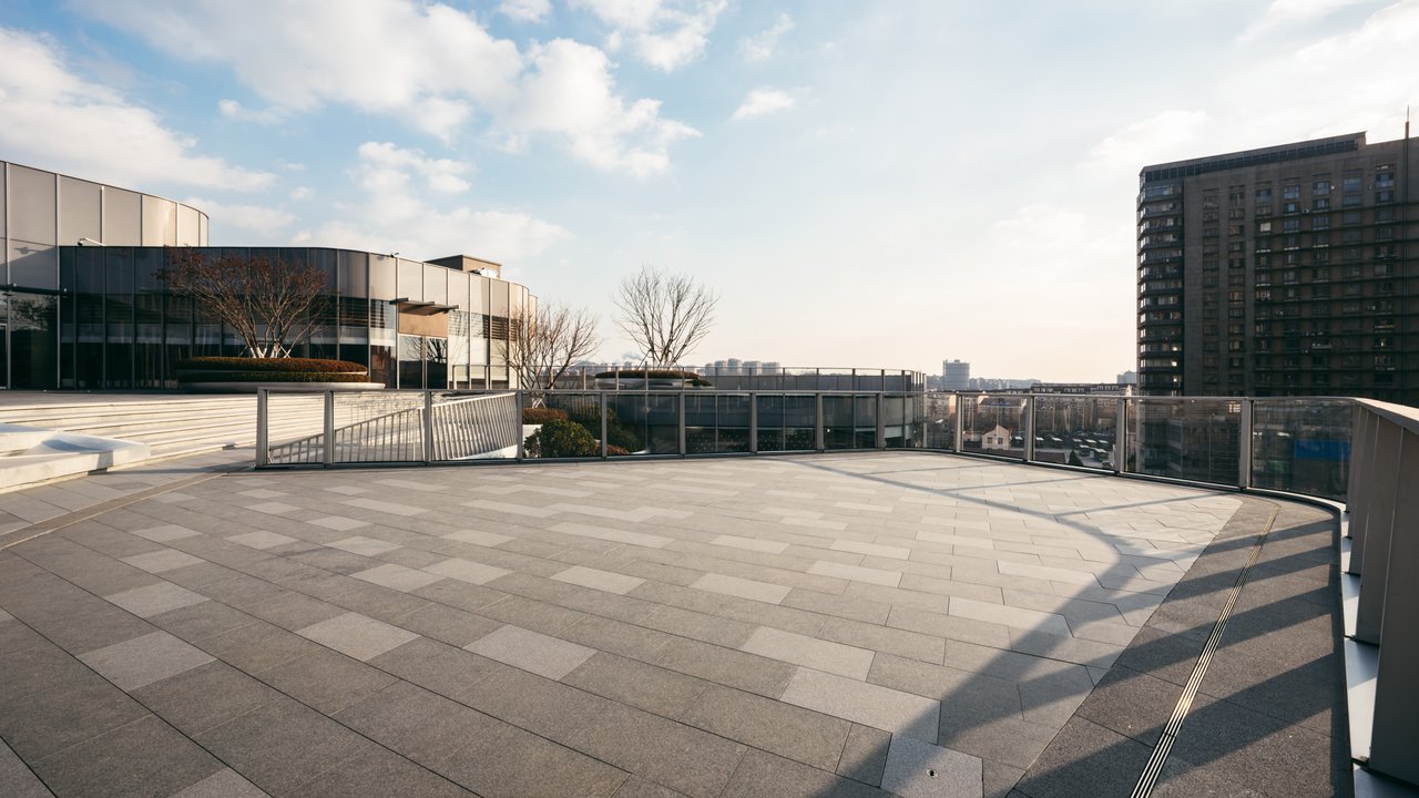 Spacious Rooftop Terrace with City View A spacious rooftop terrace with gray tiles, surrounded by modern buildings and a clear blue sky.