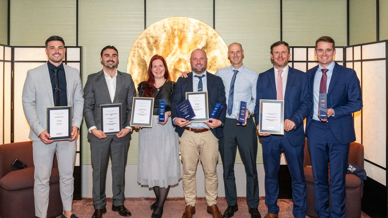 A group of seven people holding awards and certificates in a formal setting with a decorative background.