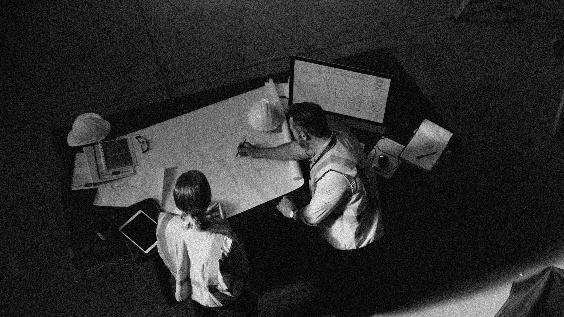 Early Engagment Black and White High angle shot of two engineers going over a blueprint together in an industrial place of work