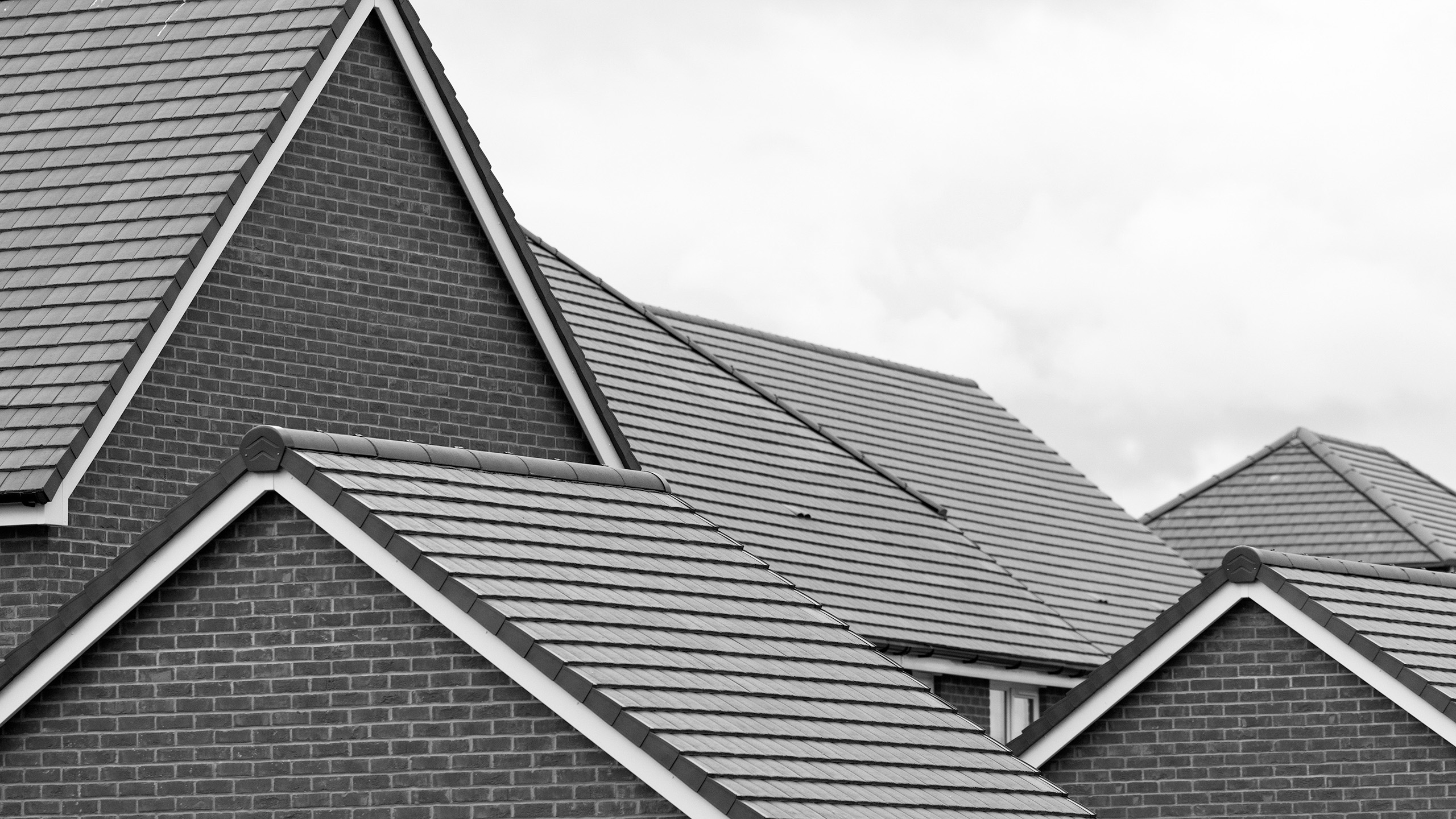 Training Course Questions and Answers Close-up of multiple rooftops with gray tiles and brick walls under a cloudy sky.